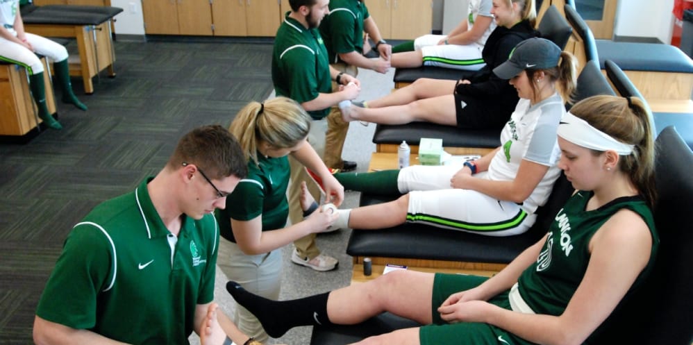 Sports medicine practitioners wrapping tape on softball player's ankles